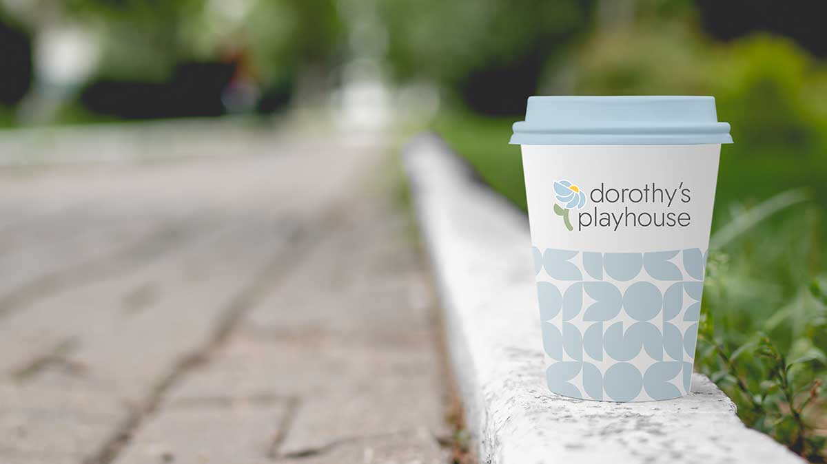 Disposable coffee cup sitting on a curb on a summer day with geometric pattern and logo.