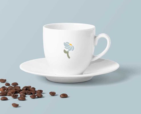 Ceramic coffee cup that is white with a blue flower logo mark in the middle