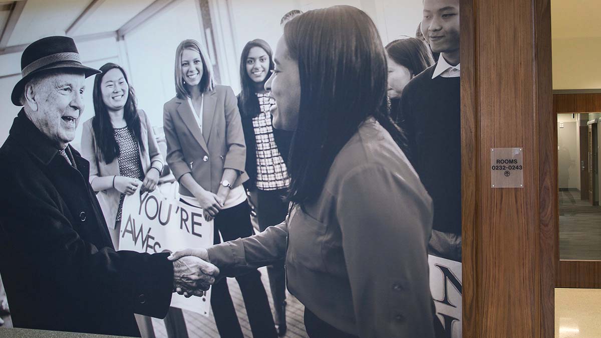 Conrad Prebys wall graphic. The wall wrap is a photo of Conrad Prebys surrounded by students and shaking one student's hand. It's black and white.