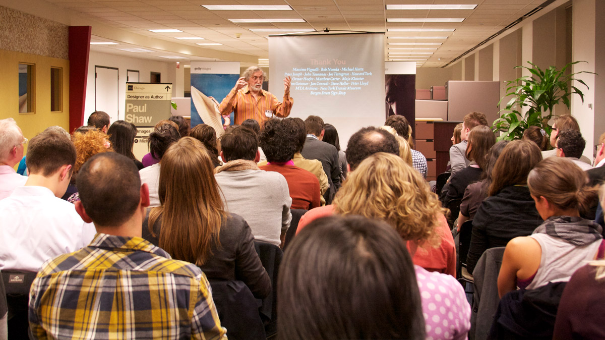 Man standing and giving a presentation to a large crowd at Designer as Author series