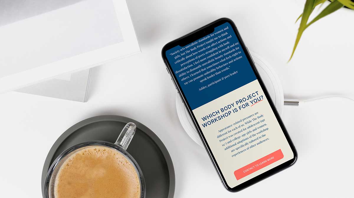 A mobile phone with a website on it, next to a cup of coffee